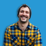 Portrait of Shea Pestell, certified life coach in North Vancouver, wearing a blue and yellow plaid shirt on a blue background.
